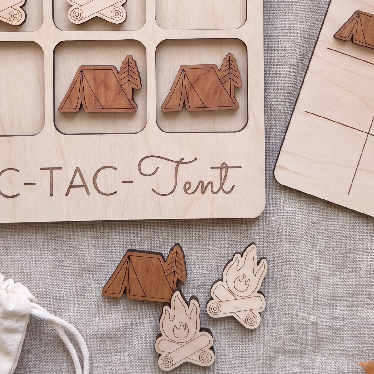 a wooden game board with a tic-tac game design, along with several wooden game pieces depicting camping scenes.