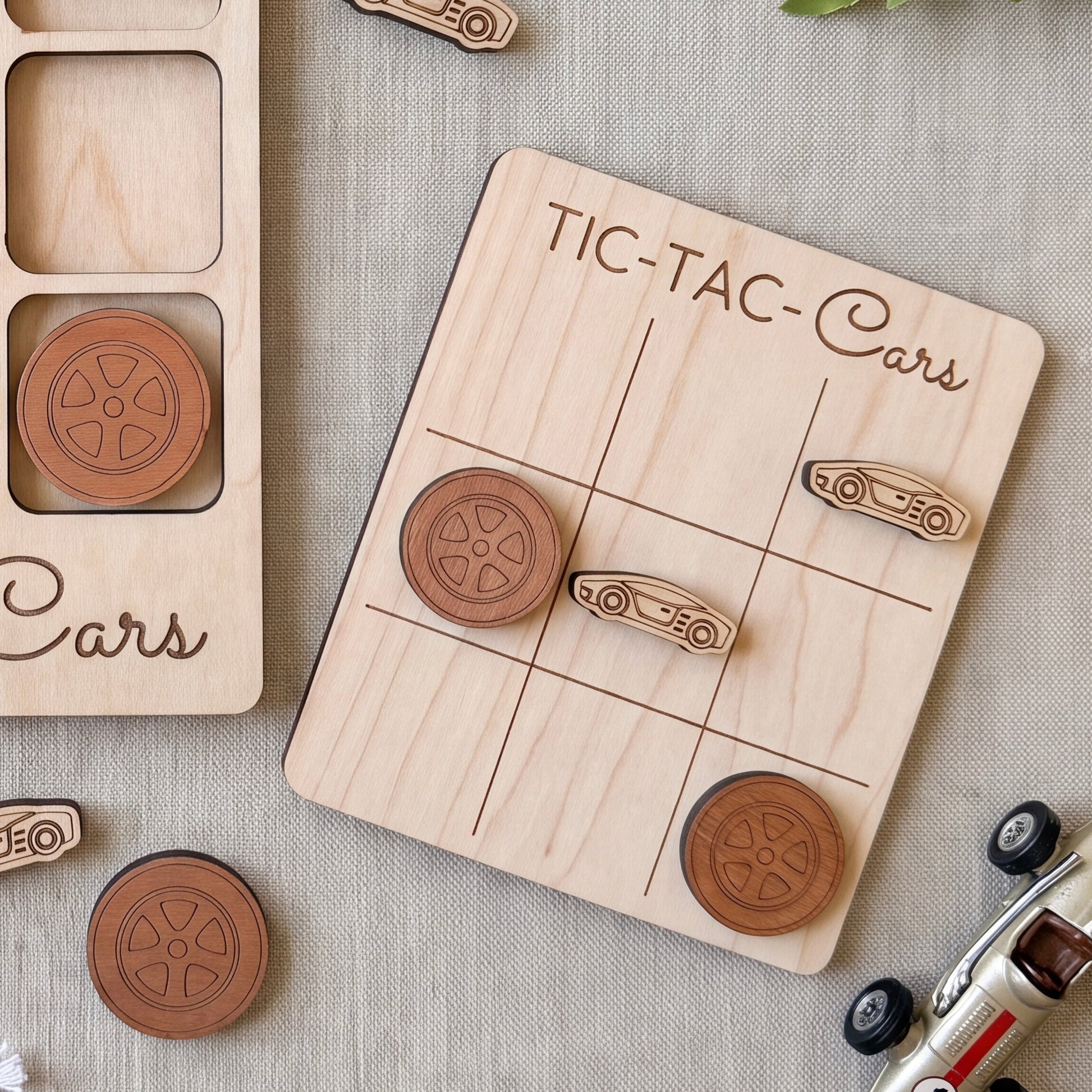 a wooden tic-tac game board with car-themed tiles, and there are several wooden car tiles scattered around the board.