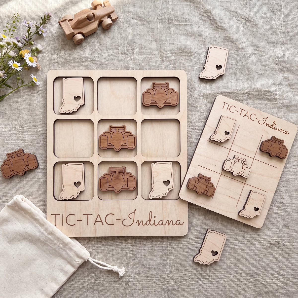a wooden tic-tac game set with wooden pieces shaped like Indiana state symbols, along with a wooden toy car and a white cloth.