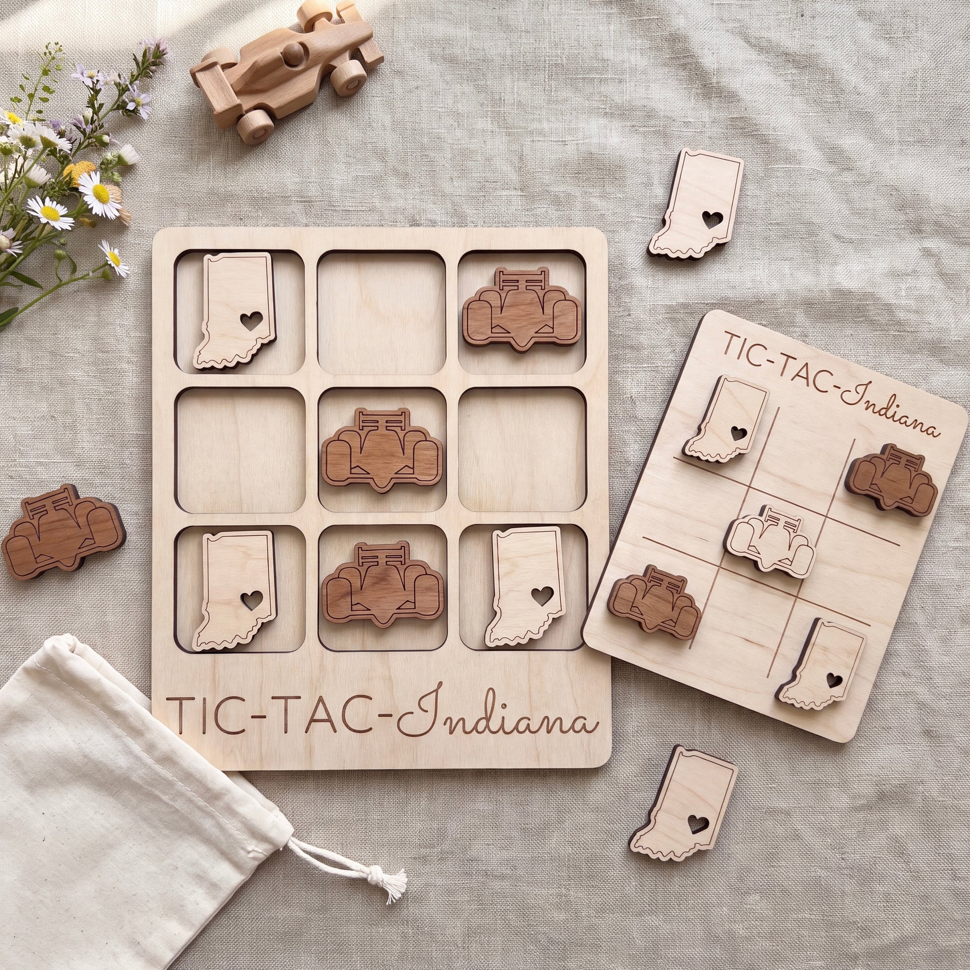 a wooden tic-tac game set with wooden pieces shaped like Indiana state symbols, along with a wooden toy car and a white cloth.