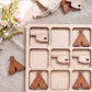 a wooden tic-tac-toe board with wooden cut-out shapes representing the states of Oklahoma and Texas. There are also wooden cut-out shapes resembling teepees, which are placed on the board.