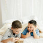 two boys laying on a bed playing with a board game