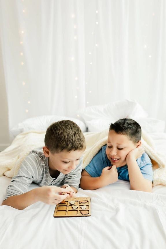 two boys laying on a bed playing with a board game