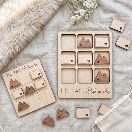 a wooden tic-tac game set with wooden pieces shaped like mountains, placed on a beige cloth. There are also some wooden pieces with hearts on them, and a white cloth with flowers.