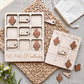 a wooden tic-tac game board and a tic-tac card with wooden pieces, both labeled "TIC-TAC-KENTUCKY". The game board and card are placed on a woven placemat, and there are some flowers visible in the background.