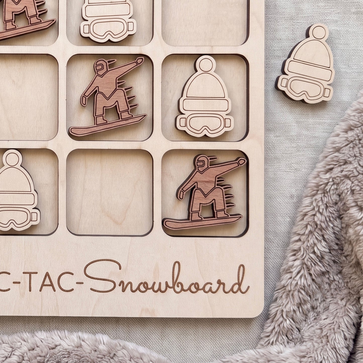A wooden tic-tac-toe board with snowboard-themed tiles, featuring a snowboarder and snowboard icons.