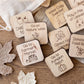a collection of wooden stickers or labels with various fall-themed illustrations, such as apples, pumpkins, leaves, and a sweater.