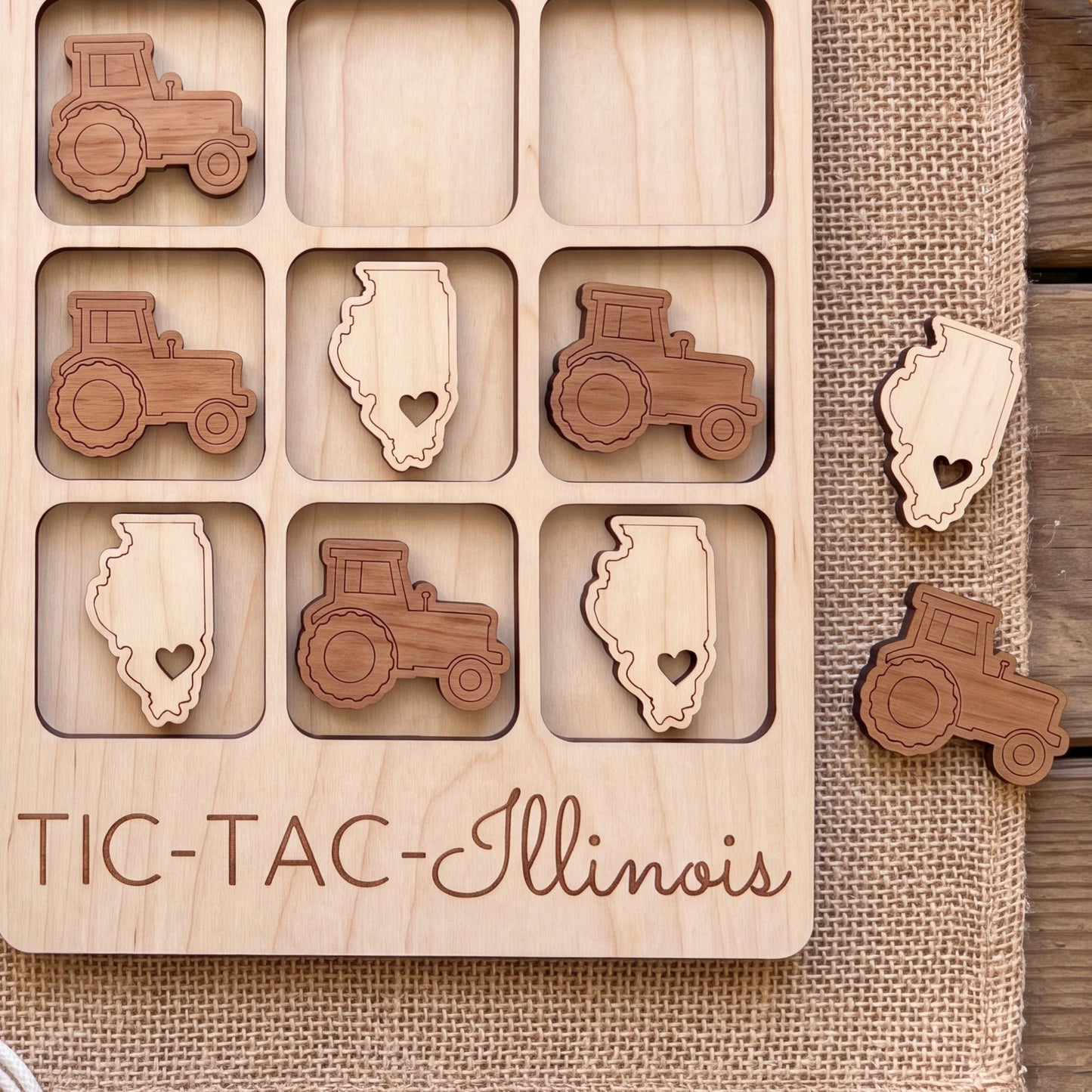 A wooden game board with a tractor and an Illinois state map as game pieces, along with the text "TIC-TAC- Illinois" printed on it.
