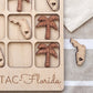 A wooden tic-tac-toe board with wooden tiles shaped like Florida state icons, including a palm tree and a heart-shaped tile.