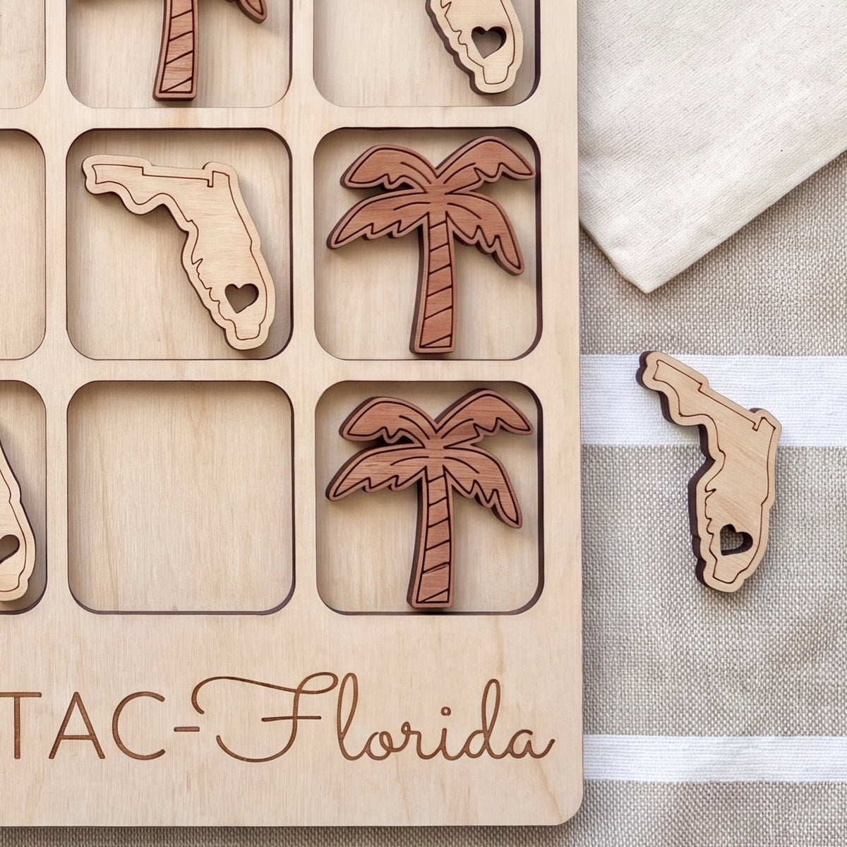 A wooden tic-tac-toe board with wooden tiles shaped like Florida state icons, including a palm tree and a heart-shaped tile.