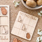 a wooden tic-tac game with Idaho state symbols on it, along with a bowl of potatoes and some flowers.