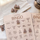 a wooden bingo board with various camping-related questions and bingo cards, along with some wooden bingo pieces on a white cloth.