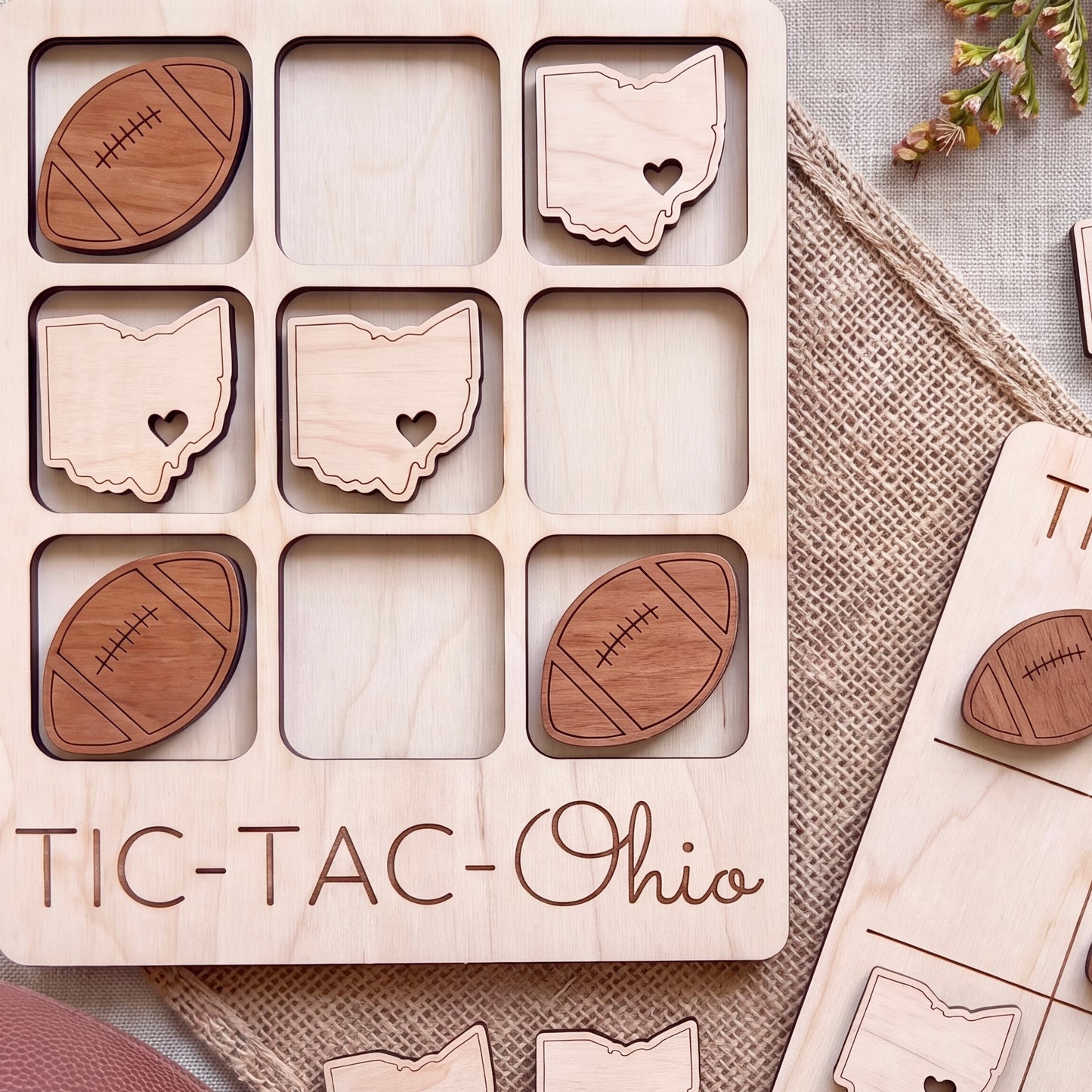 A wooden tic-tac game board with the word "TIC-TAC-OHIO" printed on it, along with various wooden game pieces shaped like footballs and state maps.