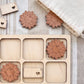 a wooden tic-tac-toe board with wooden pieces shaped like flowers, placed on a beige cloth.