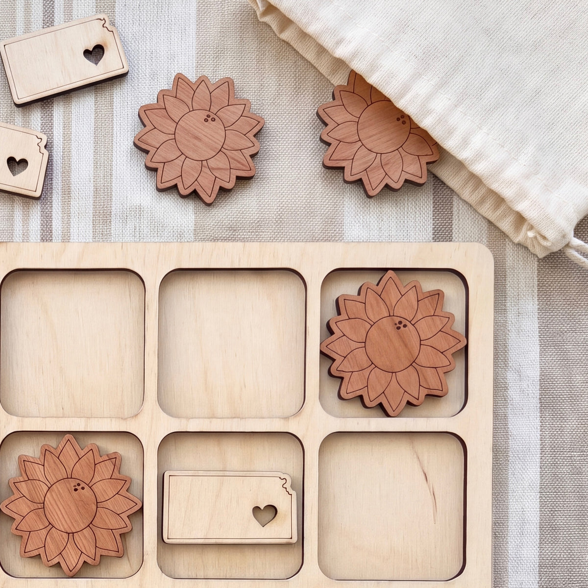 a wooden tic-tac-toe board with wooden pieces shaped like flowers, placed on a beige cloth.