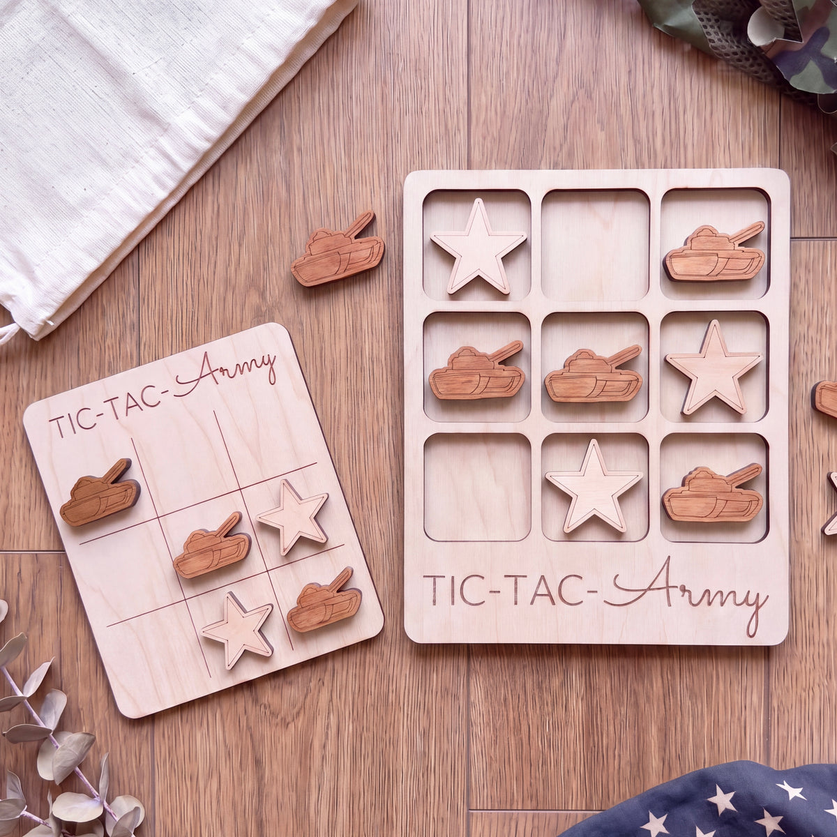 a wooden tic-tac-army game with wooden pieces shaped like tanks and stars, placed on a wooden surface alongside a white cloth.