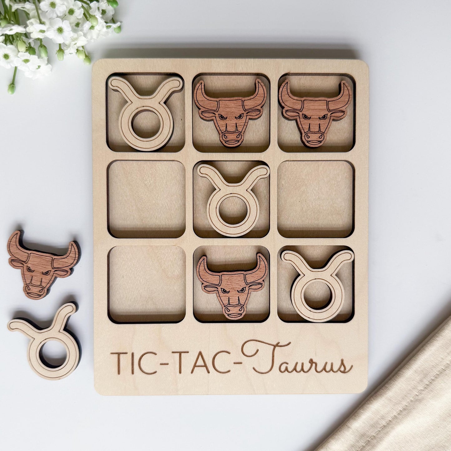 A wooden tic-tac game board with cut-out images of taurus symbols, including a bull, a lion, and a horse.