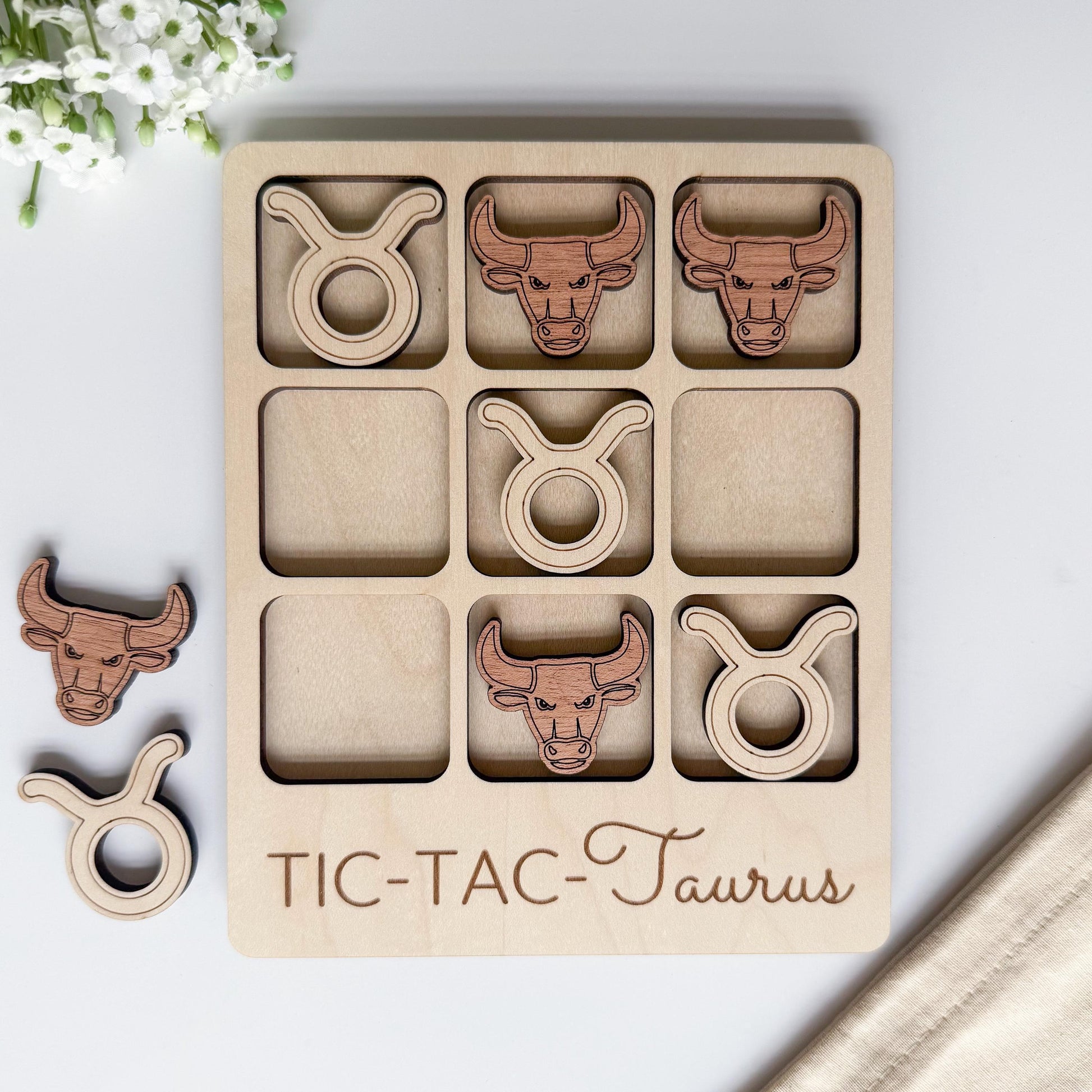 A wooden tic-tac game board with cut-out images of taurus symbols, including a bull, a lion, and a horse.