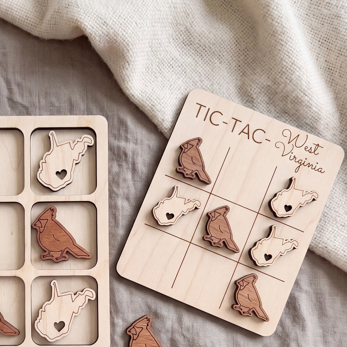 a wooden tic-tac game board with bird-shaped tiles, and a blanket with a patterned texture is visible in the background.