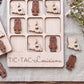 A wooden tic-tac game board with the word "TIC-TAC-LOUISIANA" written on it, along with various wooden tiles shaped like lobsters and hearts.