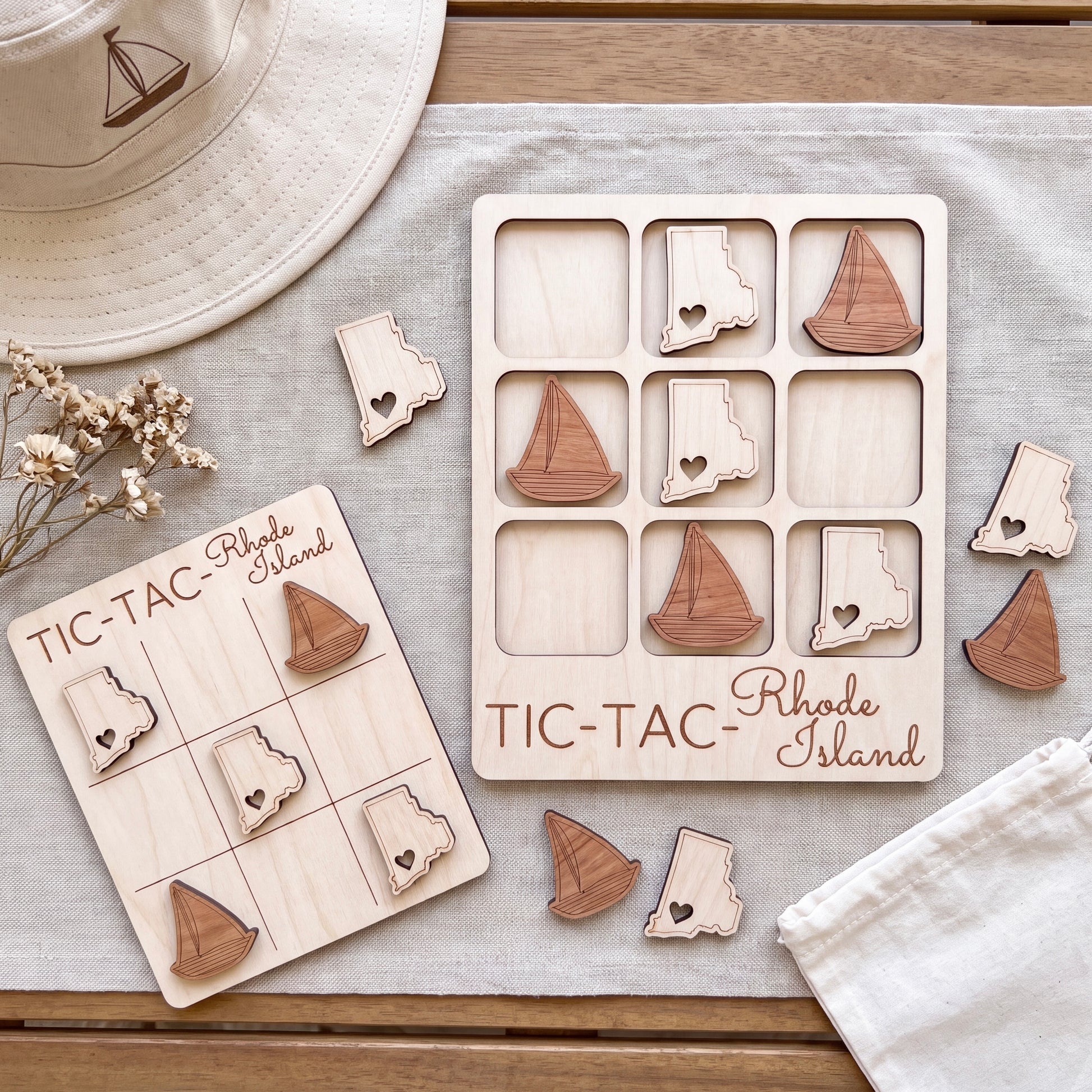 a wooden tic-tac game with Rhode Island tiles, a hat, and some flowers on a table.