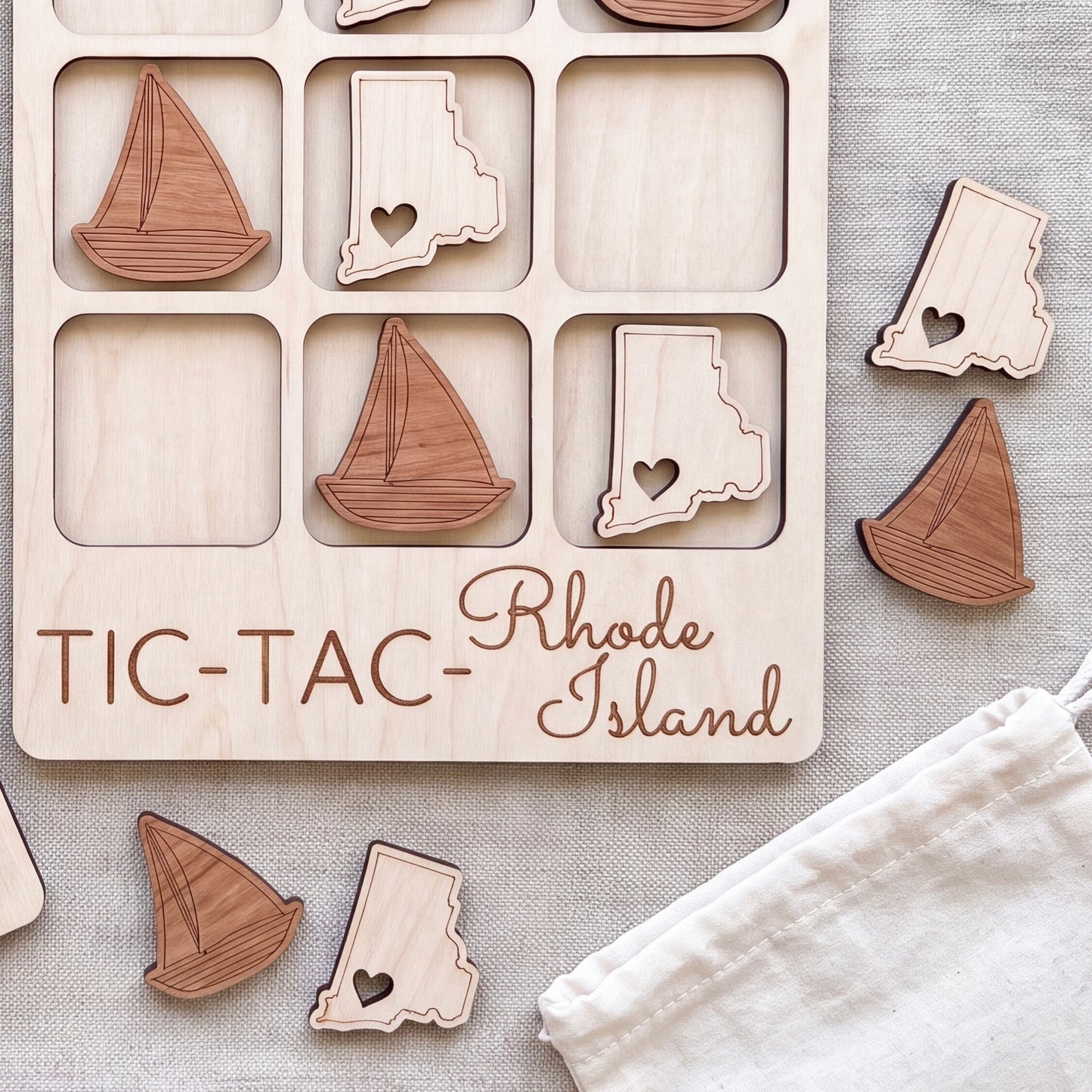 a wooden tic-tac game board with wooden pieces shaped like the states of Rhode Island, including a sailboat and a heart-shaped piece.