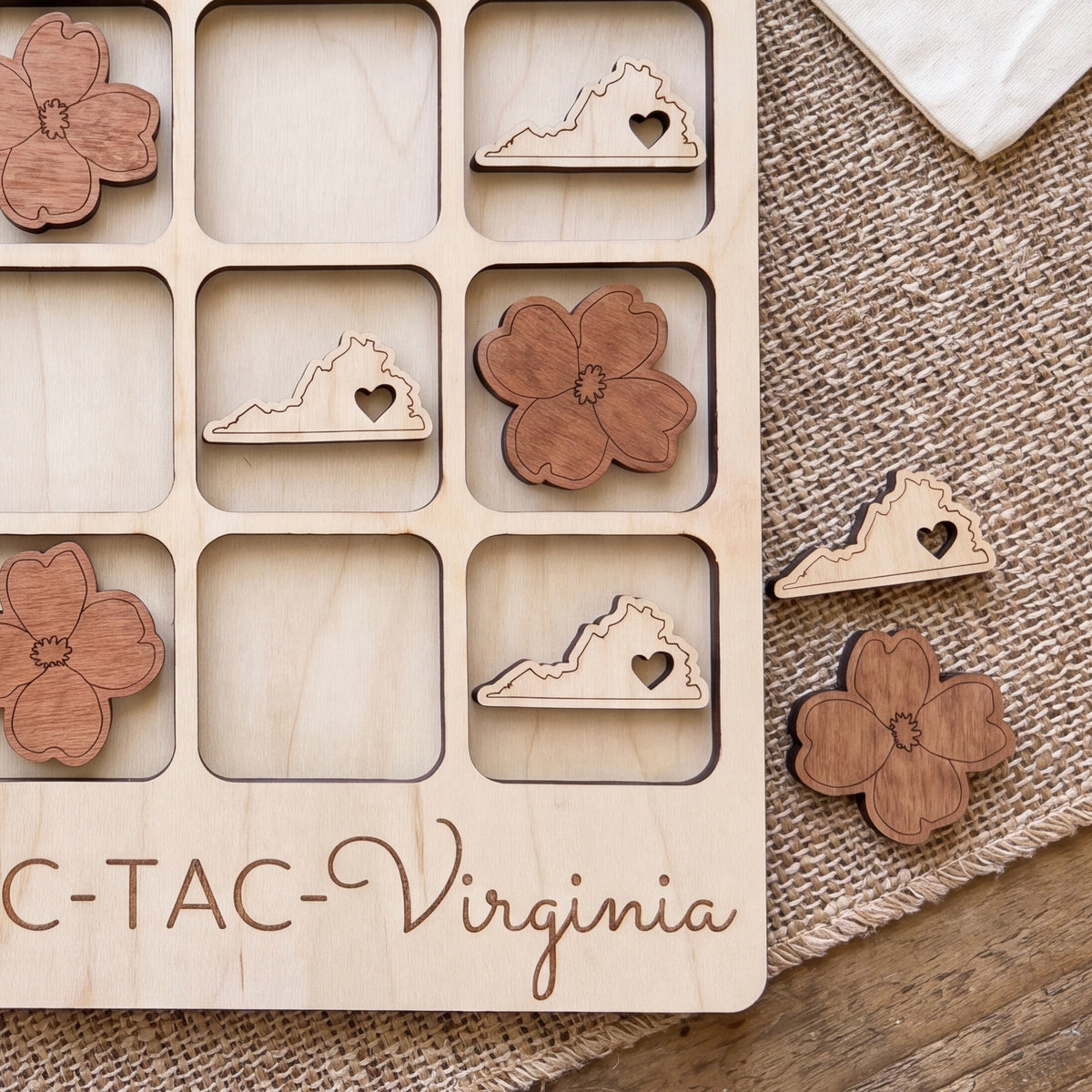 A wooden tic-tac board with wooden pieces shaped like flowers and the word "VIRGINIA" written on it.