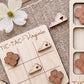 a wooden tic-tac game board with wooden pieces shaped like flowers, including a white flower, placed on a woven surface.