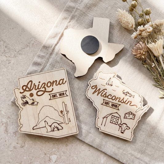 two wooden magnets shaped like the states of Arizona and Wisconsin, with decorative designs and text.