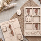 a wooden tic-tac game with a light wood texture and a woven placemat. The game has a grid with wooden pieces and a wooden board with wooden pieces. There are also some wooden pieces on a woven placemat.