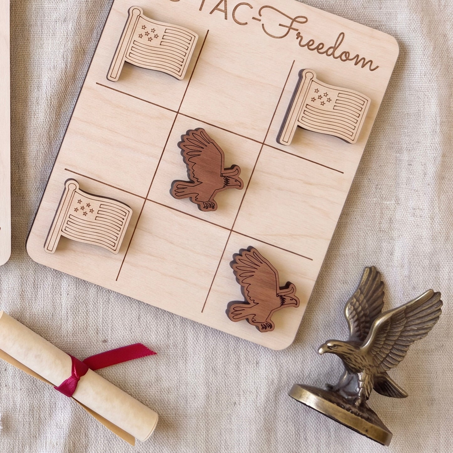 a wooden tic-tac game board with wooden eagle tiles, a rolled-up diploma, and a metal eagle figurine.