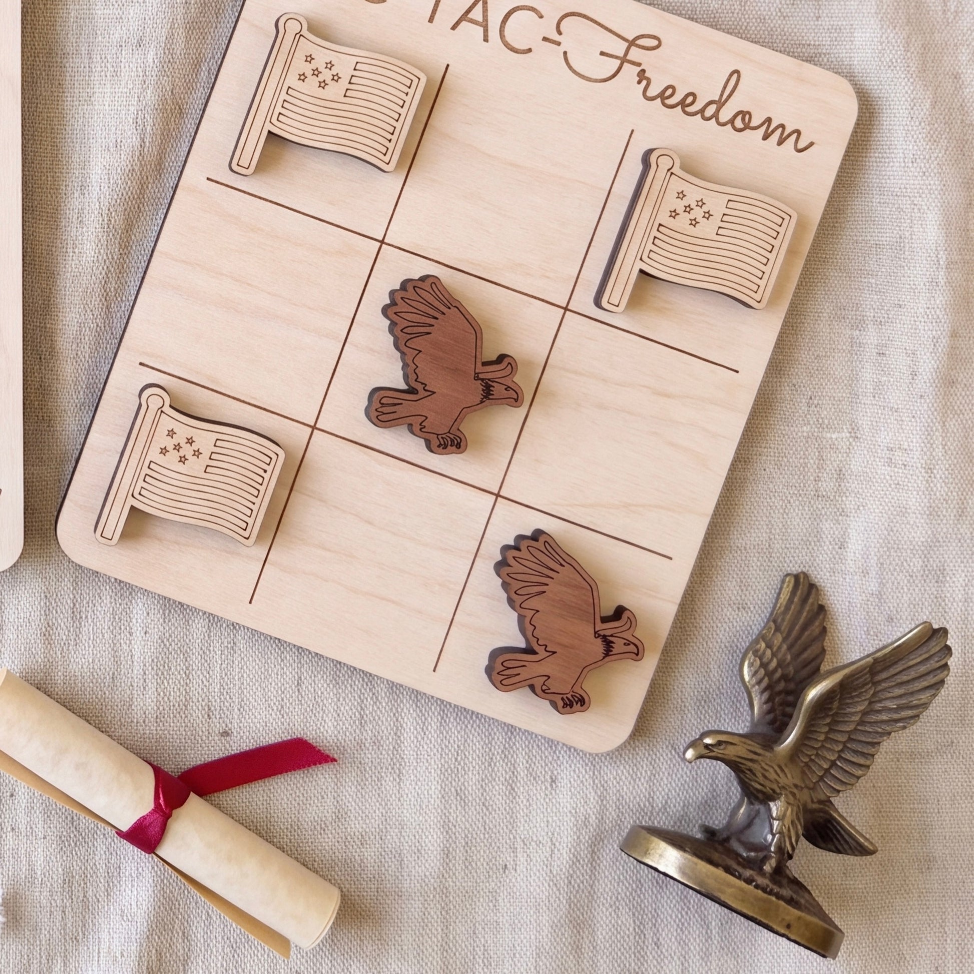 a wooden tic-tac game board with wooden eagle tiles, a rolled-up diploma, and a metal eagle figurine.