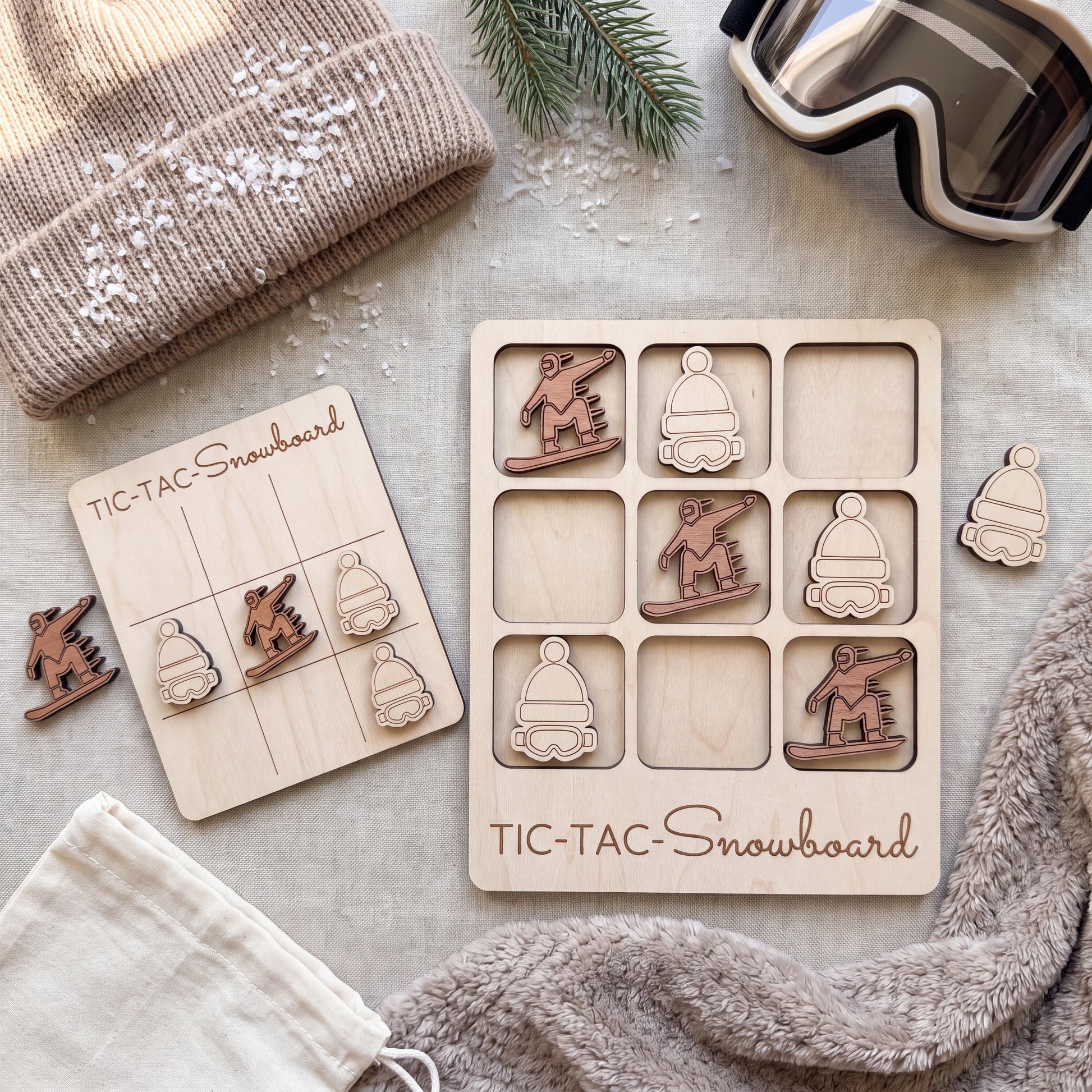 a wooden snowboard game with a tic-tac board, a pair of wooden snowboard stickers, and a pair of goggles.