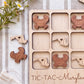 A wooden tic-tac game board with wooden crab and lobster pieces, along with a bouquet of flowers and a striped cloth in the background.