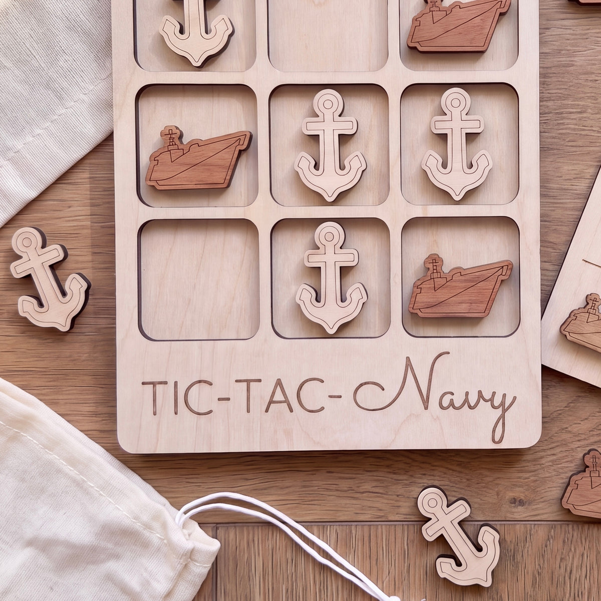 A wooden tic-tac-toe game board with wooden anchors and ships on it, along with some additional wooden anchors and ships.