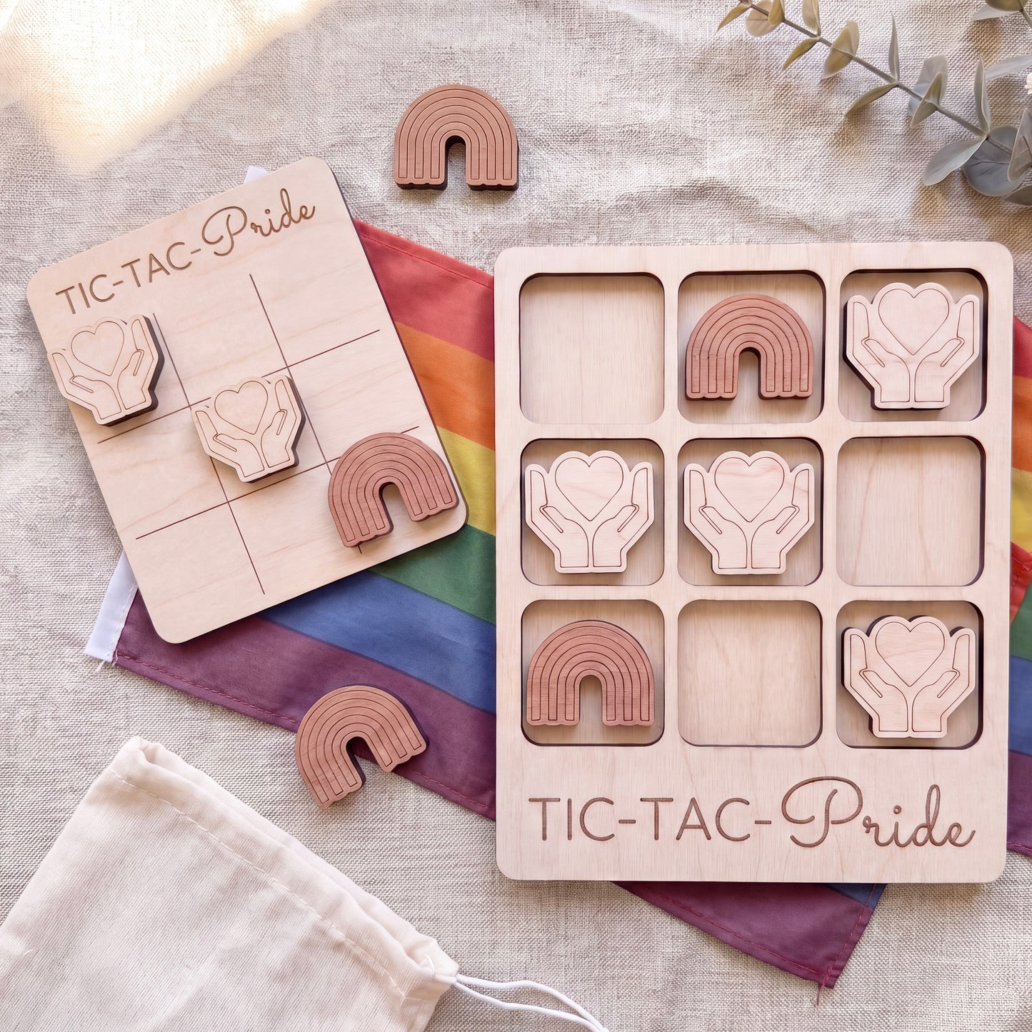 a wooden tic-tac game with a rainbow flag and wooden hearts as game pieces. The game is labeled "TIC-TAC-Pride".