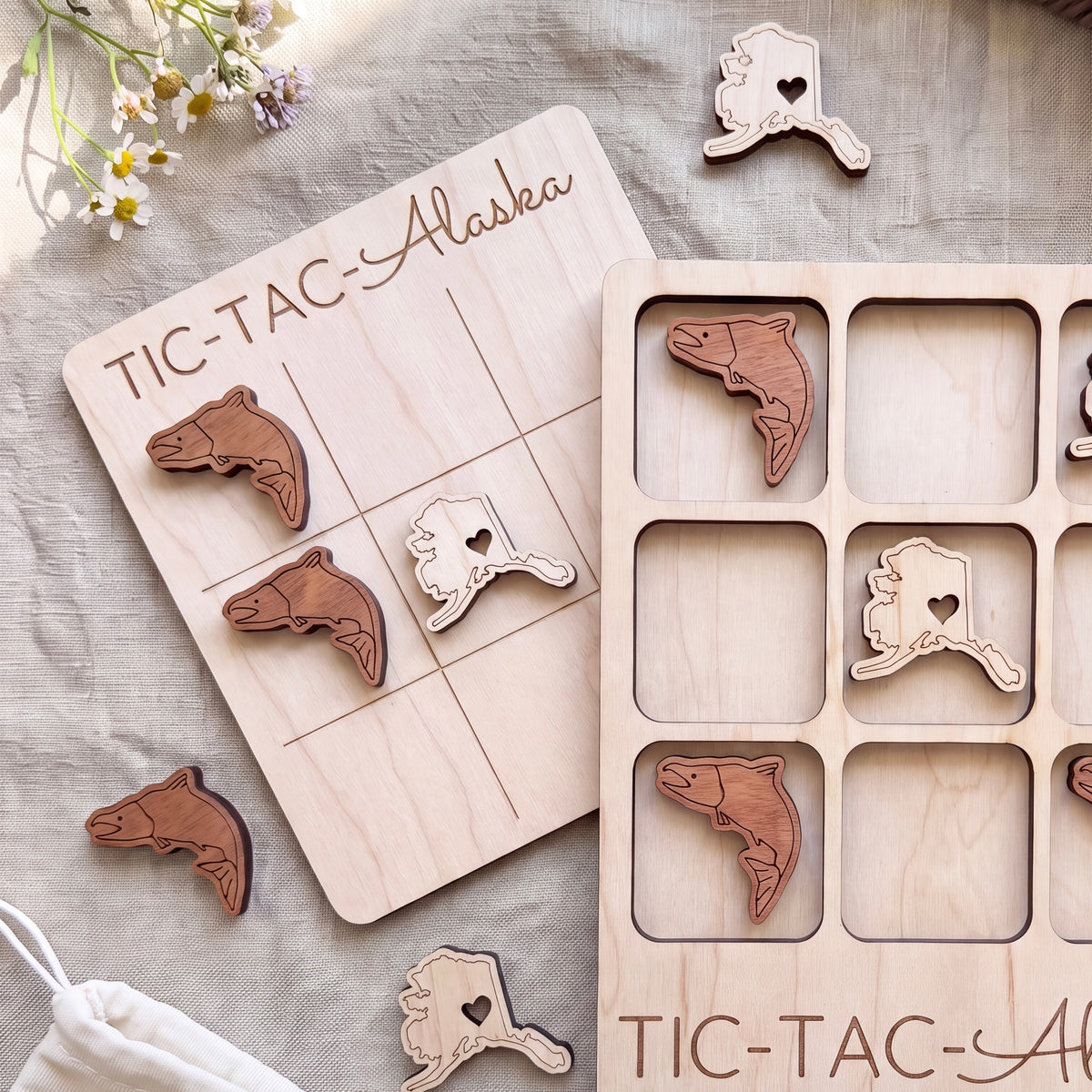 a wooden tic-tac game with a light wood finish, and there are several wooden tic-tac pieces with Alaska state designs on them.