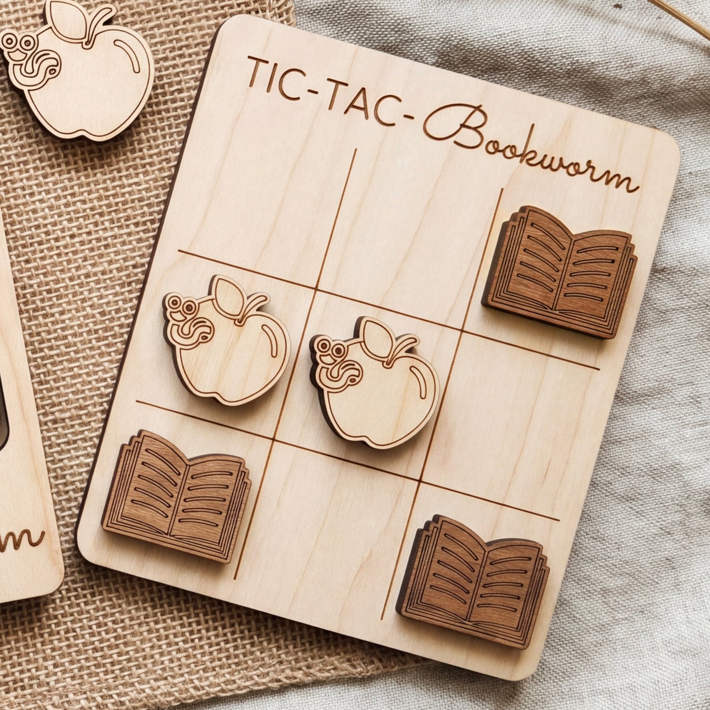 A wooden tic-tac board game with book-themed tiles, featuring a book worm and an open book.