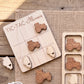 a wooden tic-tac game board with tractor-themed tiles, and there are additional wooden tractor tiles on a burlap surface.