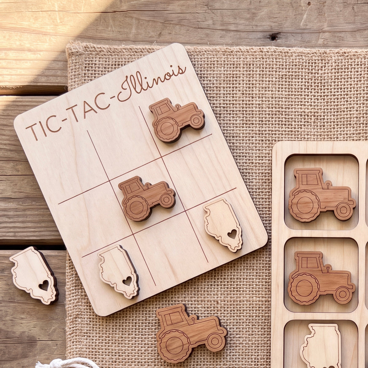 a wooden tic-tac game board with tractor-themed tiles, and there are additional wooden tractor tiles on a burlap surface.