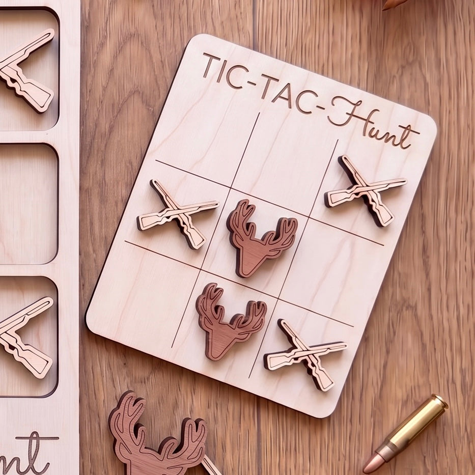 a wooden tic-tac hunt game with deer heads and crossed guns as game pieces, placed on a wooden surface alongside a bullet.