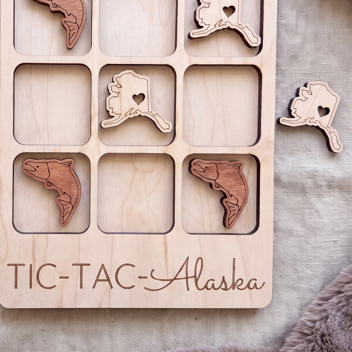 A wooden game board with a custom inscription, featuring wooden game pieces shaped like fish and the word "Alaska" written on the board.