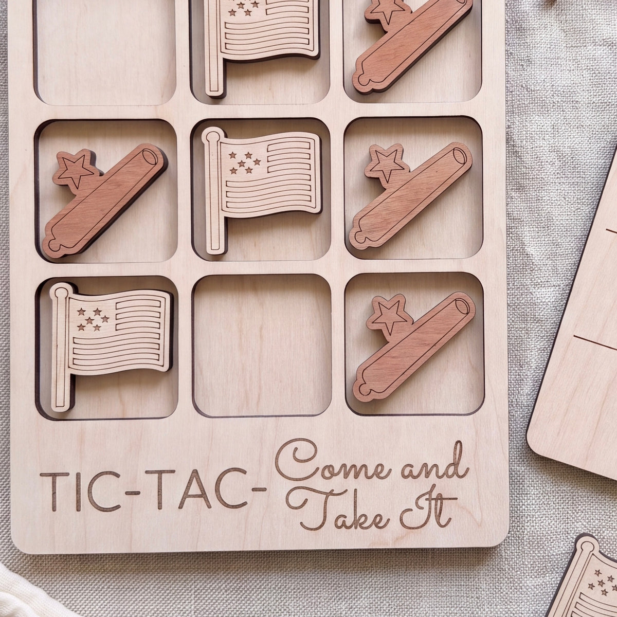 A wooden tic-tac game board with wooden pieces shaped like flags and stars, along with the text "C-TAC-Take It" printed on the board.