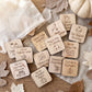 a collection of wooden tags with various fall-themed activities and instructions, such as "Go to Nature Walk", "Go to Farmer's Market", "Go to Wear Cozy Sweater", "Go to Play in Pile of Leaves", "Go on Hayride", "Donate to Food Bank", "Carve a Pumpkin Patch", and "Go on Nature Walk". The tags are scattered on a wooden surface, with some leaves visible in the background.