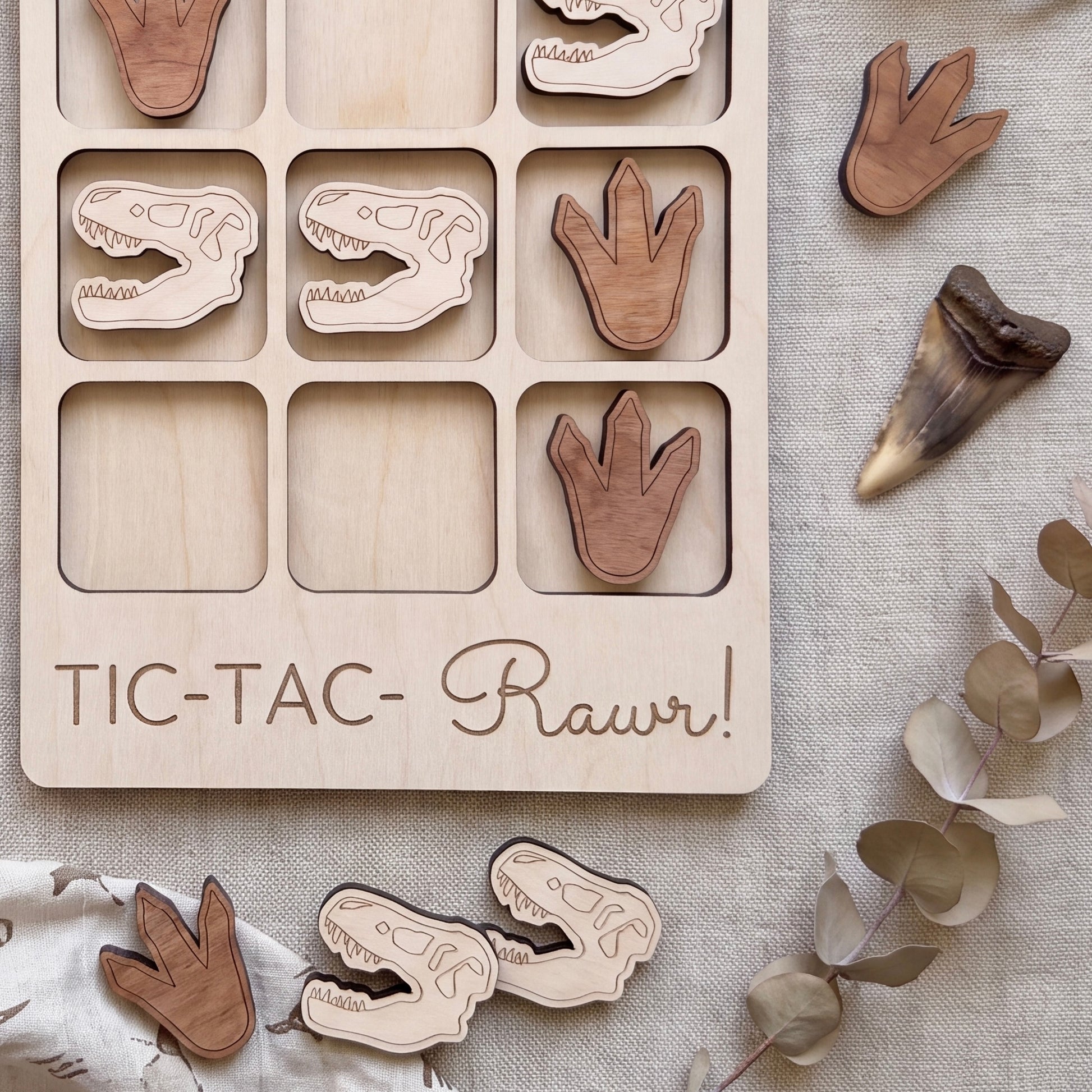 a wooden game board with dinosaur claw and tooth-shaped tiles, along with a few dinosaur claw and tooth-shaped tiles scattered around it.